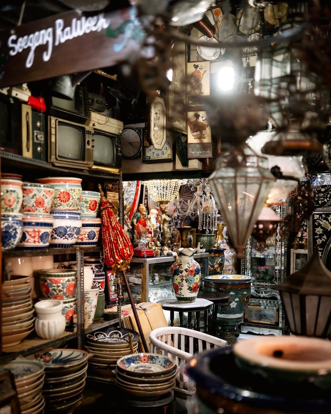 Antique shop interior filled with ceramics, vintage TVs, lamps, and various collectibles.