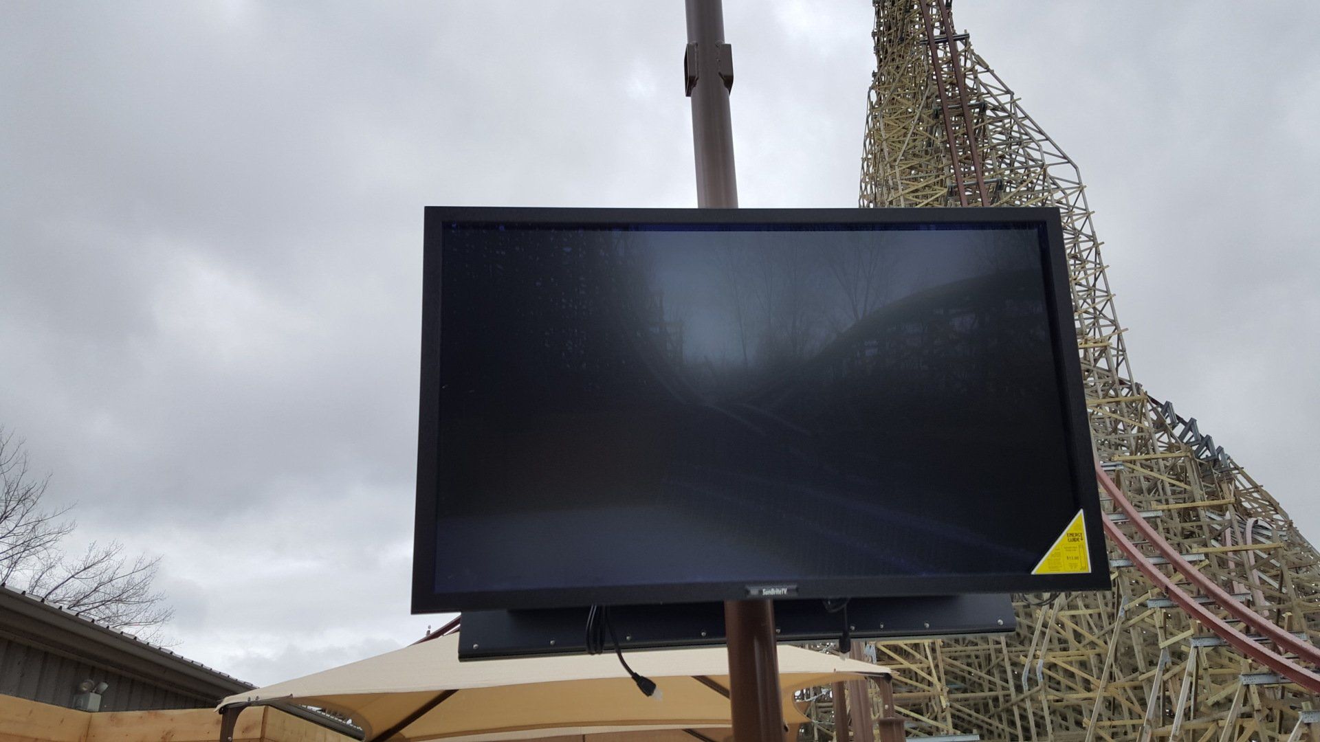 an outdoor tv at an amusement park in front of a roller coaster