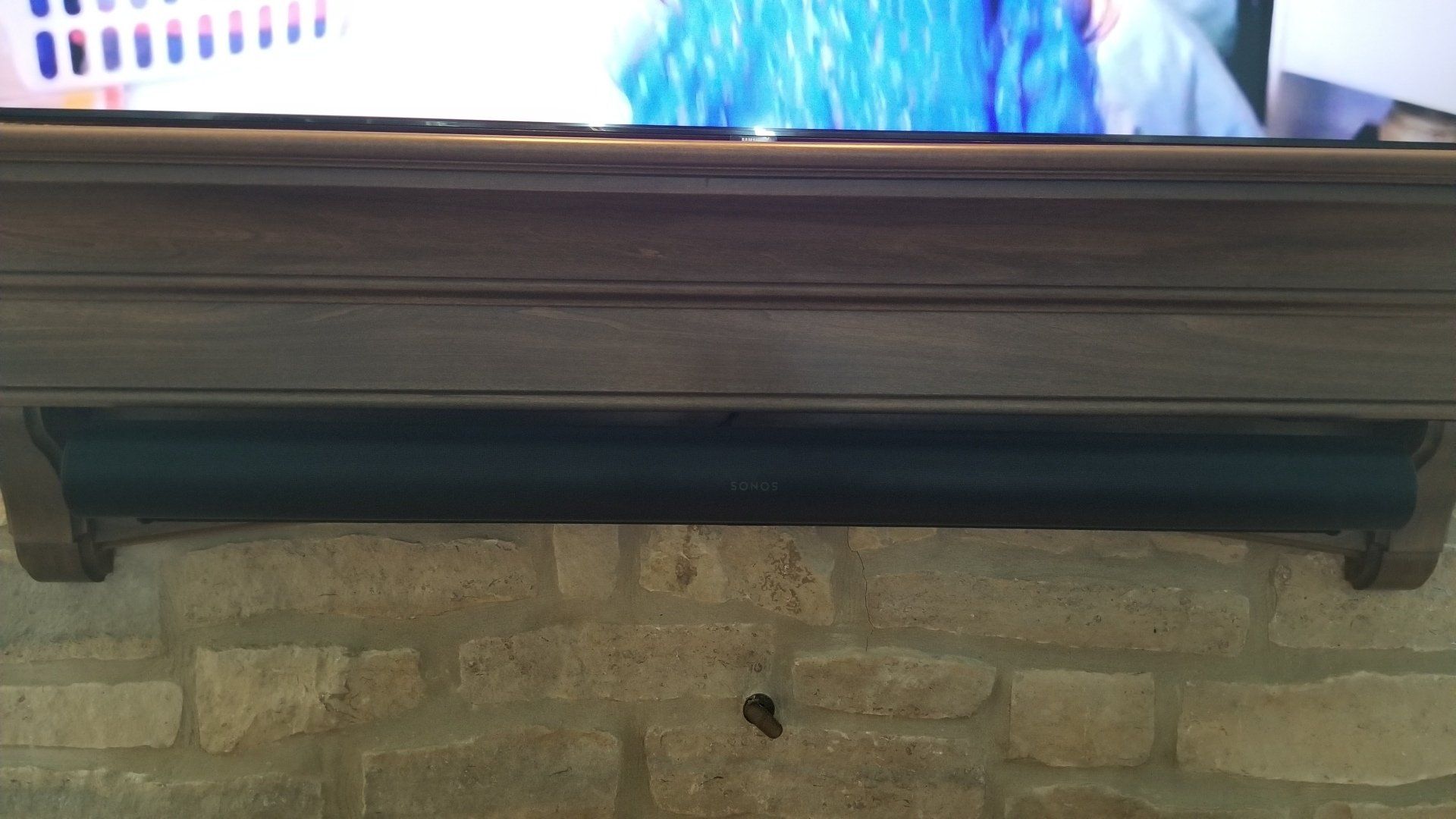 a tv is mounted on a mantle above a brick wall with a sonos arc soundbar custom mounted to the mantle. This is installed by fisher electronics in northern ohio.