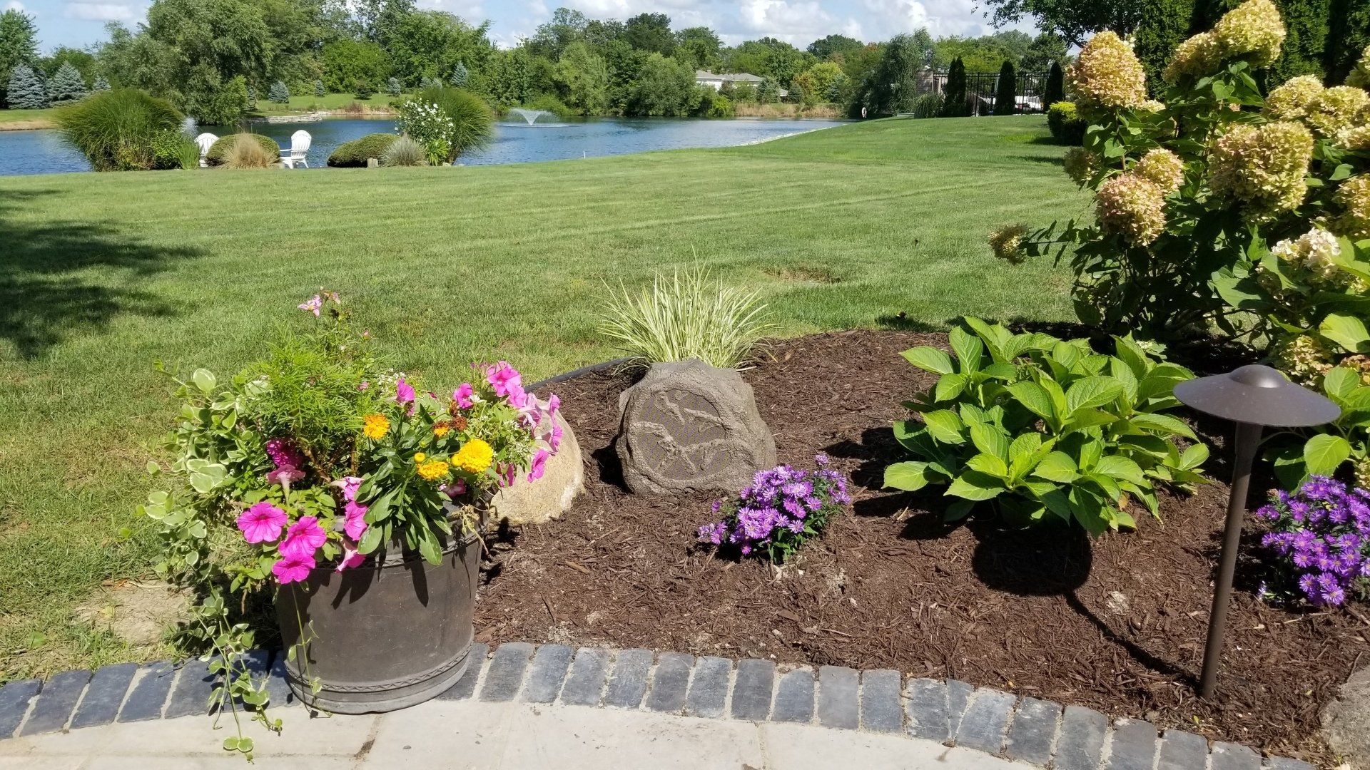 A garden with flowers, rock speakers, and a lake in the background