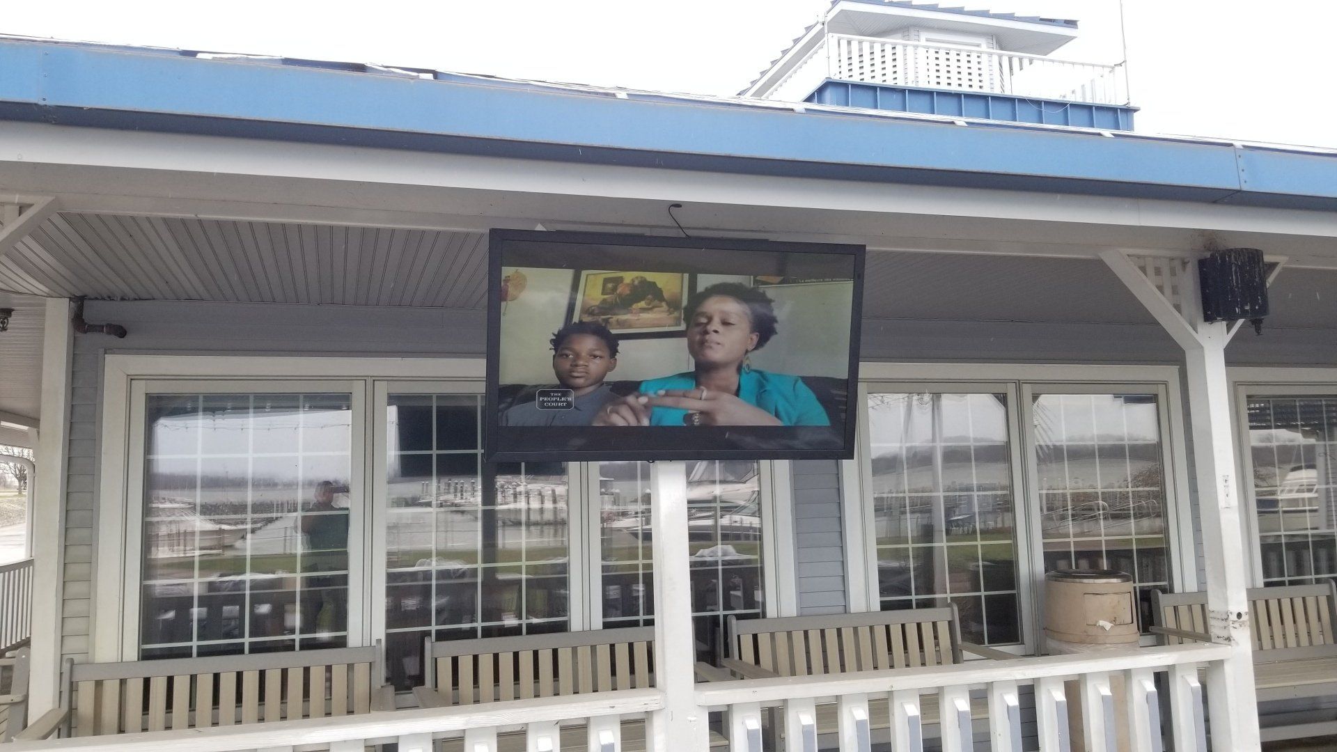 an outdoor television mounted on a porch shows a woman talking to a child