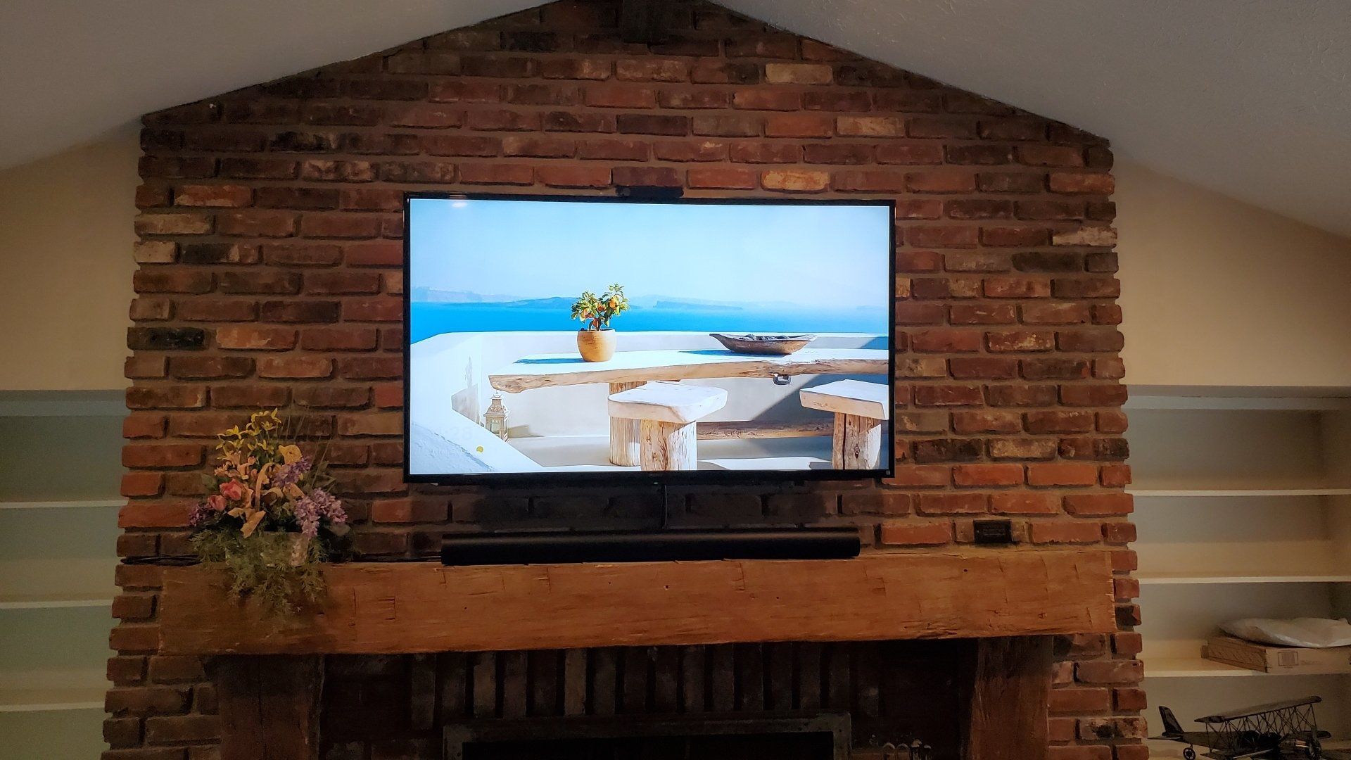 a flat screen tv is mounted to a brick wall above a fireplace with the electronics cleanly installed and hidden in a cabinet