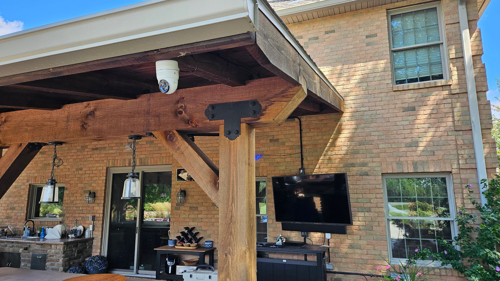 Brick house with wooden porch, outdoor TV, lights, and security camera. 