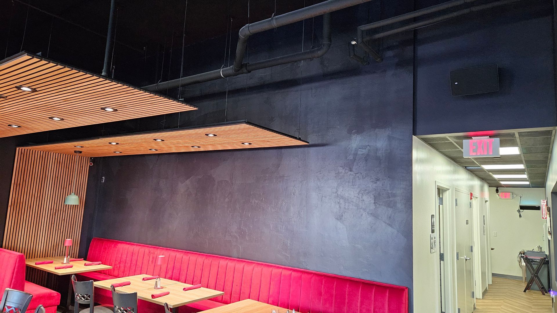 Restaurant interior with red booth seating, wooden accent panels, and a speaker installed above the hallway