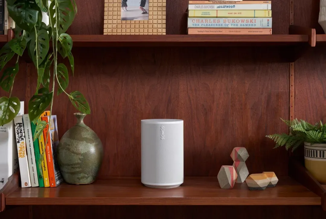 A white sonos era 100 speaker sits on a wooden shelf