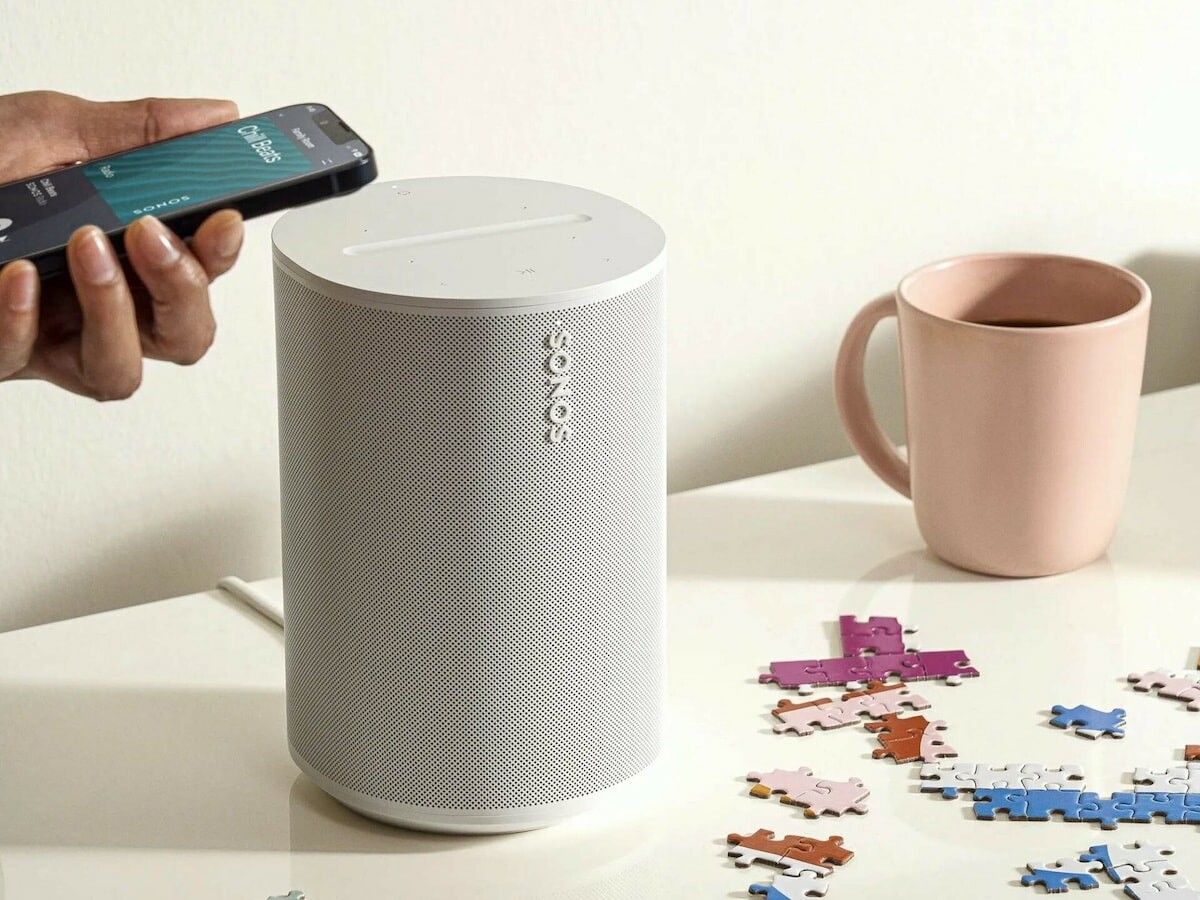a person is holding a cell phone next to a sonos wireless speaker on a table