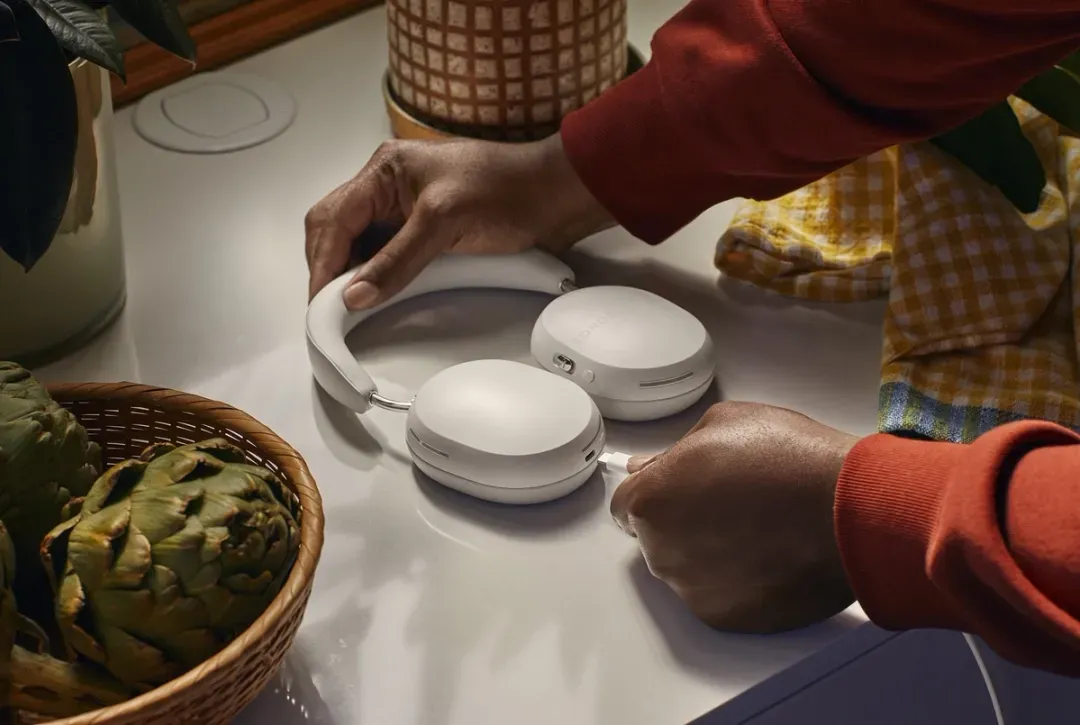 A person is holding a pair of white sonos headphones on a counter.