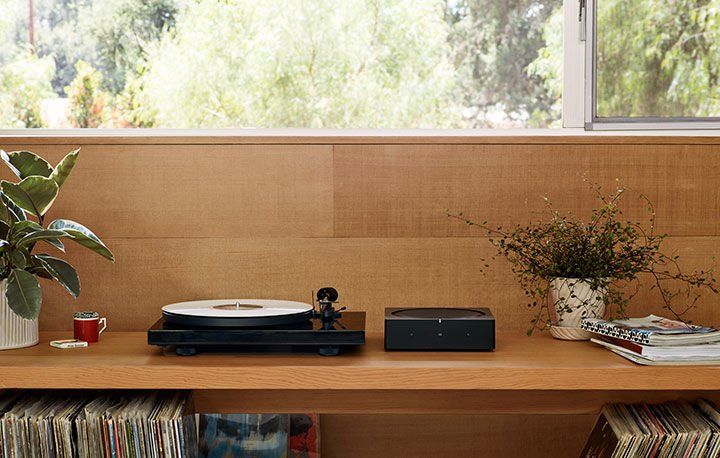 a record player is sitting on top of a wooden shelf next to a window with a sonos amp connected to it