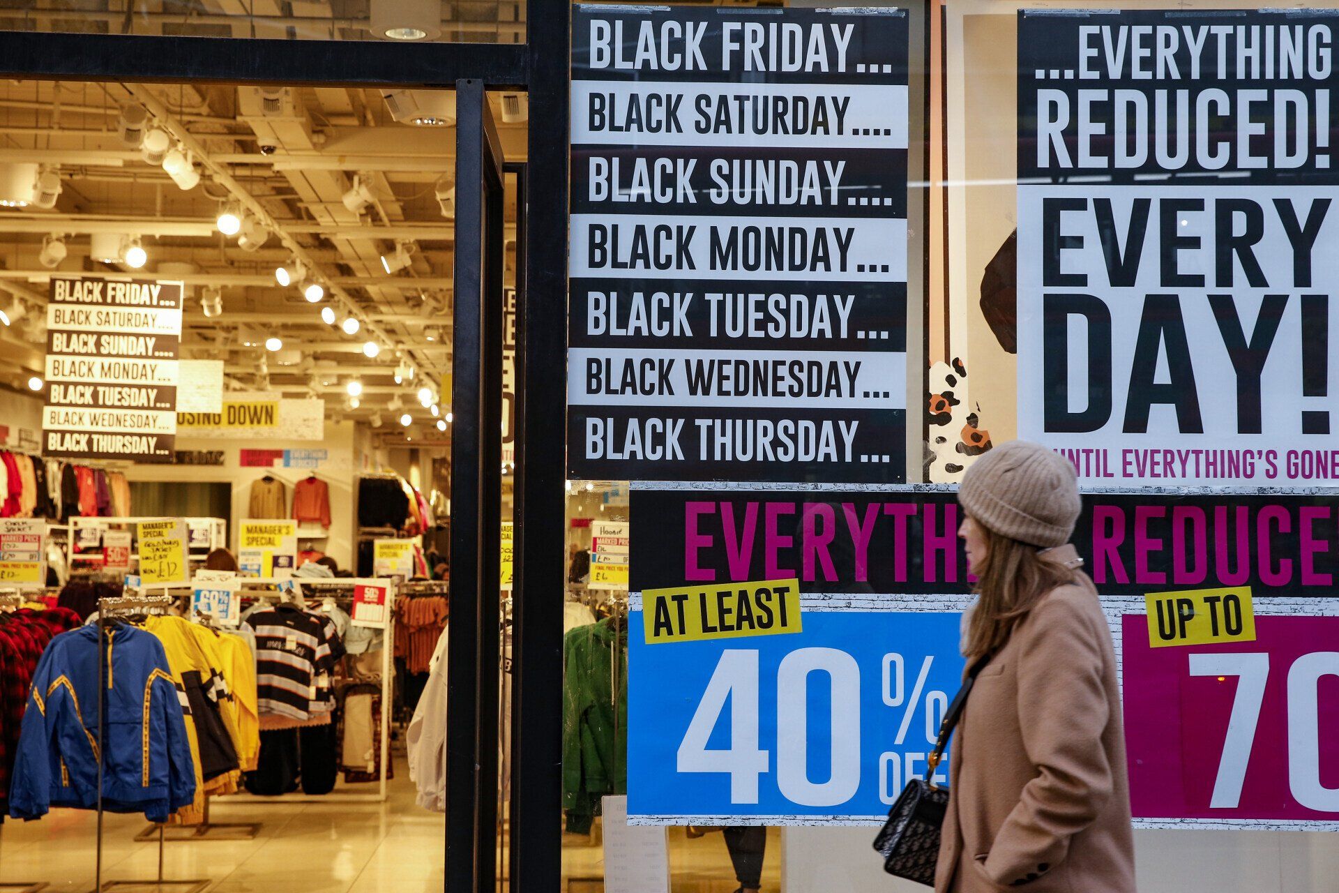 a woman walks past a store with black friday signs