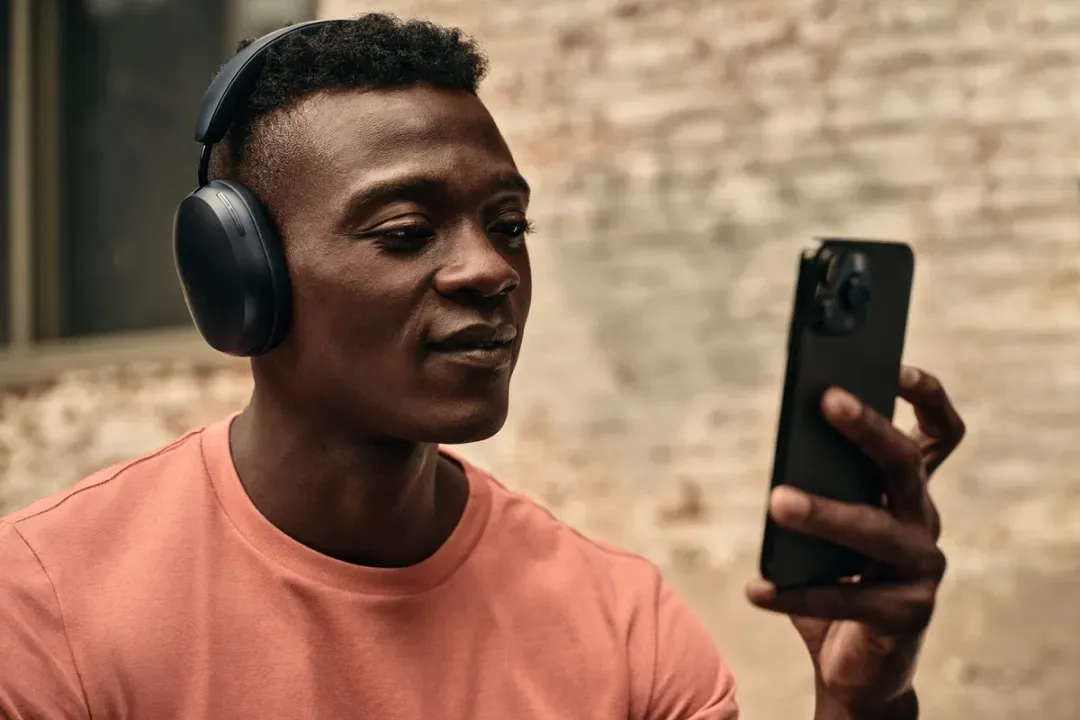 A man wearing sonos headphones is looking at his cell phone.