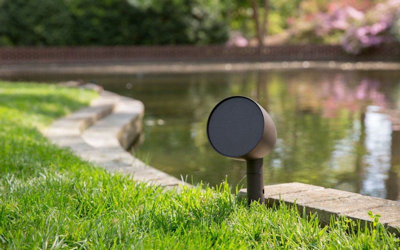 an outdoor landscape speaker is sitting in the grass next to a pond.
