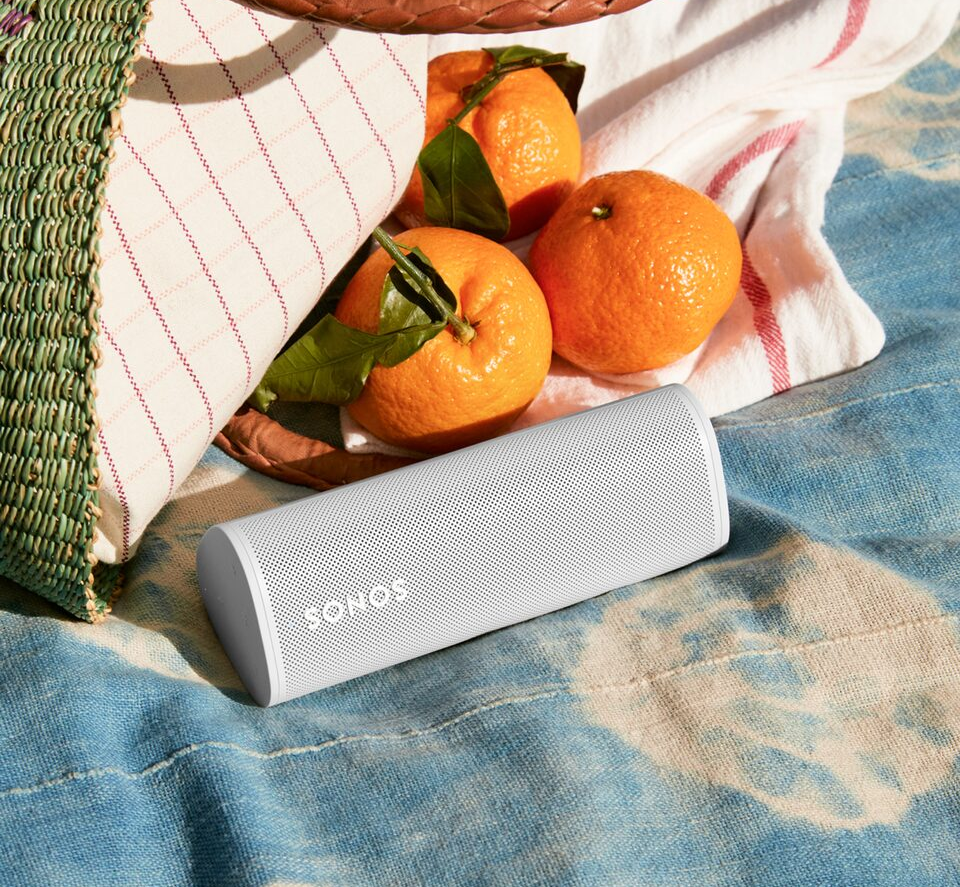 a white sonos speaker sits on a blanket next to oranges