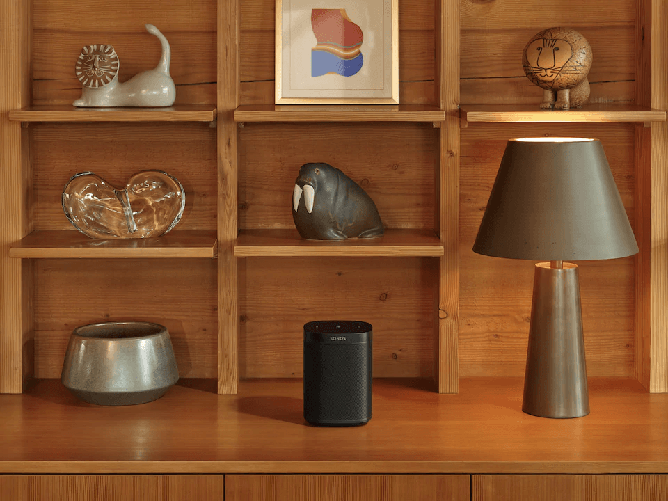 A lamp sits on a wooden shelf next to a sonos speaker