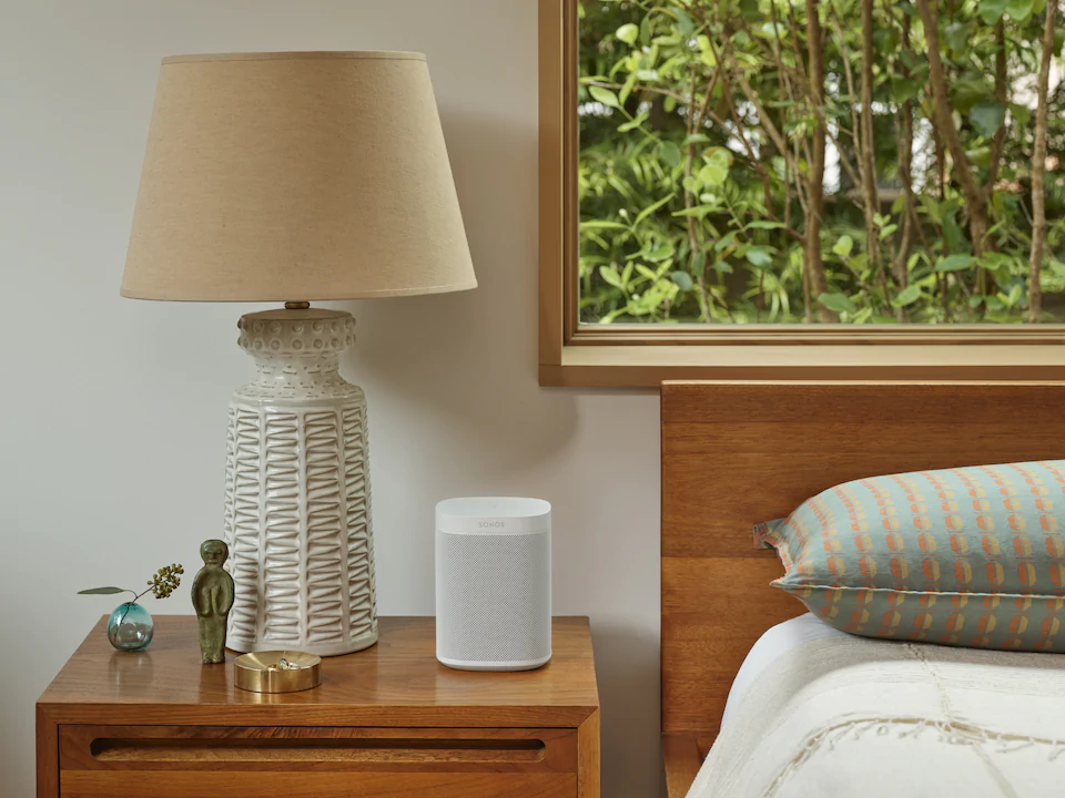 A bedroom with a lamp and a sonos speaker on a nightstand