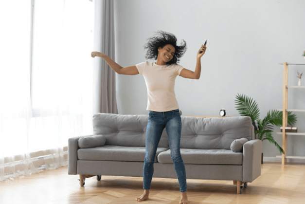 a woman is dancing in front of a couch in a living room while listening to music. She is listening to home audio installed by fisher electronics in northern ohio