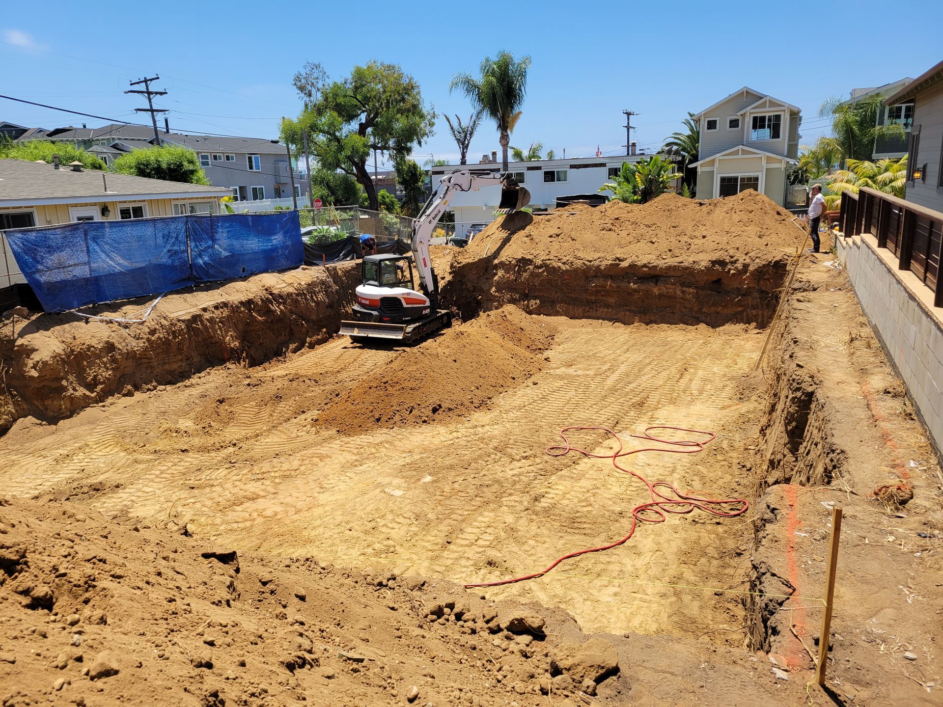 Construction site with excavator digging a foundation in a residential area.