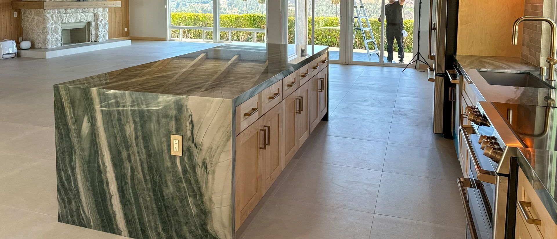 Modern kitchen with a large island with green stone countertop and wooden cabinets.