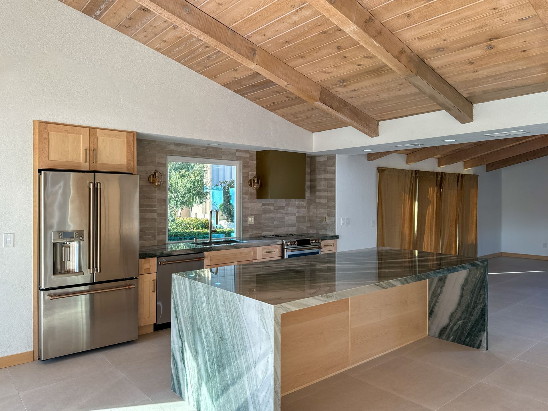 Kitchen with wooden ceiling beams, stainless steel fridge, granite island, and wood cabinets.