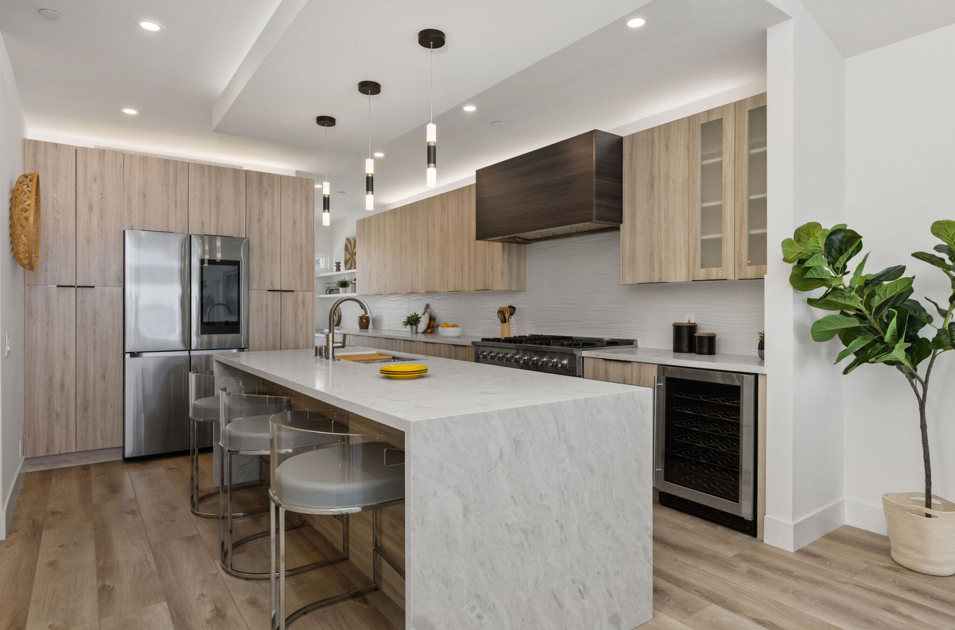 Modern kitchen with light wood cabinets, stainless steel appliances, and a marble island with seating.