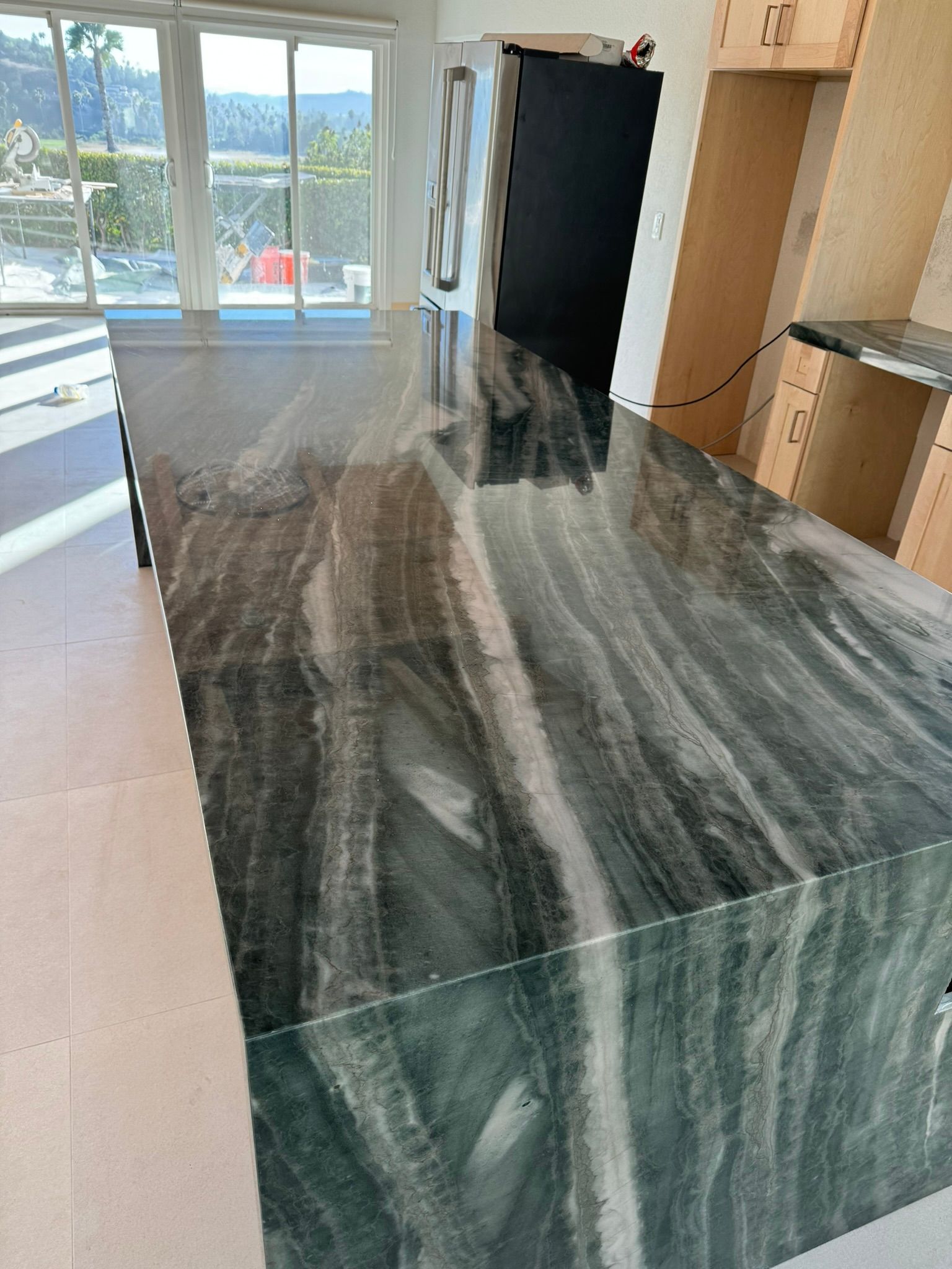 Kitchen island with gray and white veined countertop, stainless steel appliances, and wood cabinets.