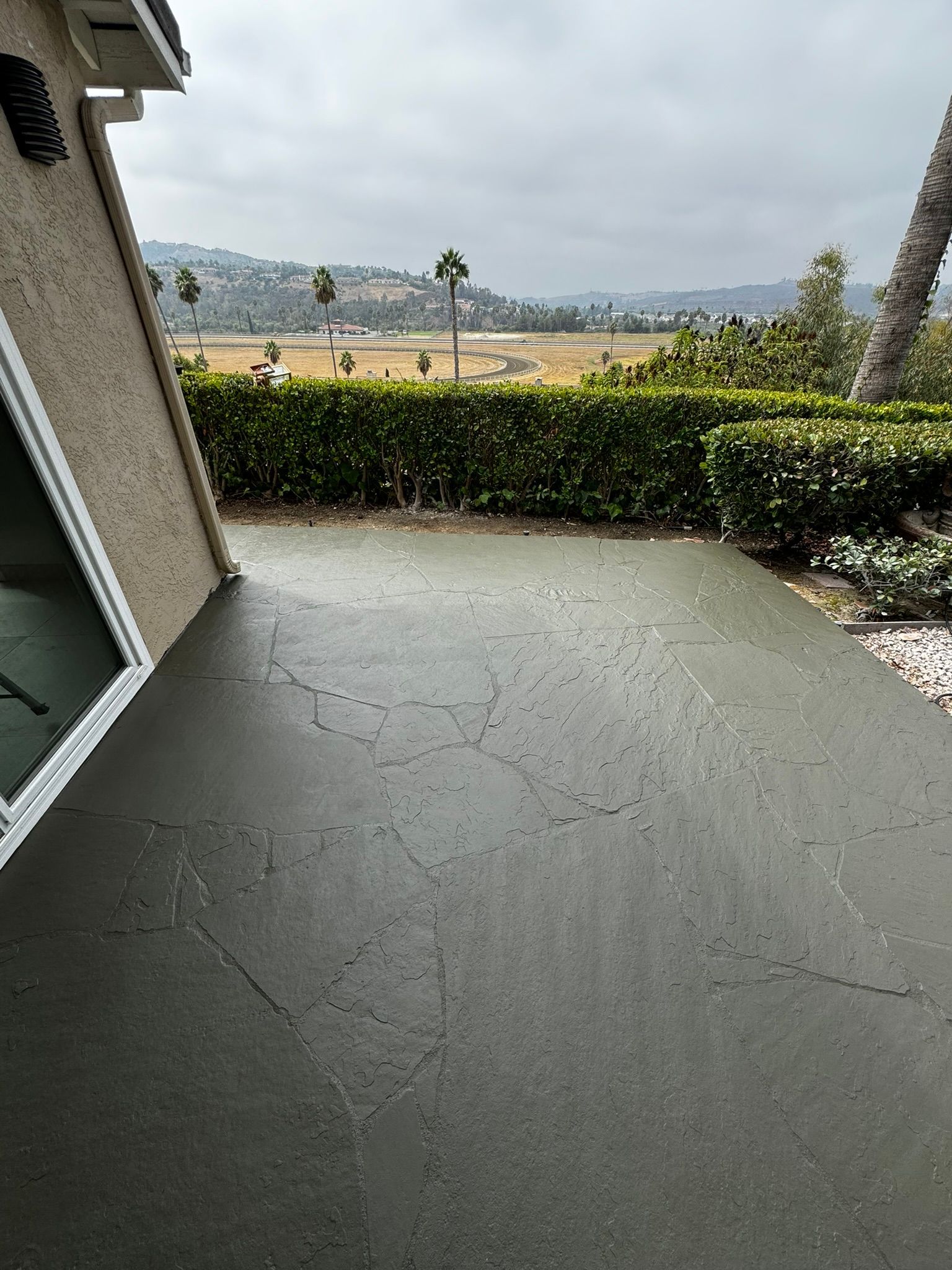 Newly poured gray concrete patio with cracks, view of greenery, and hills under overcast sky.