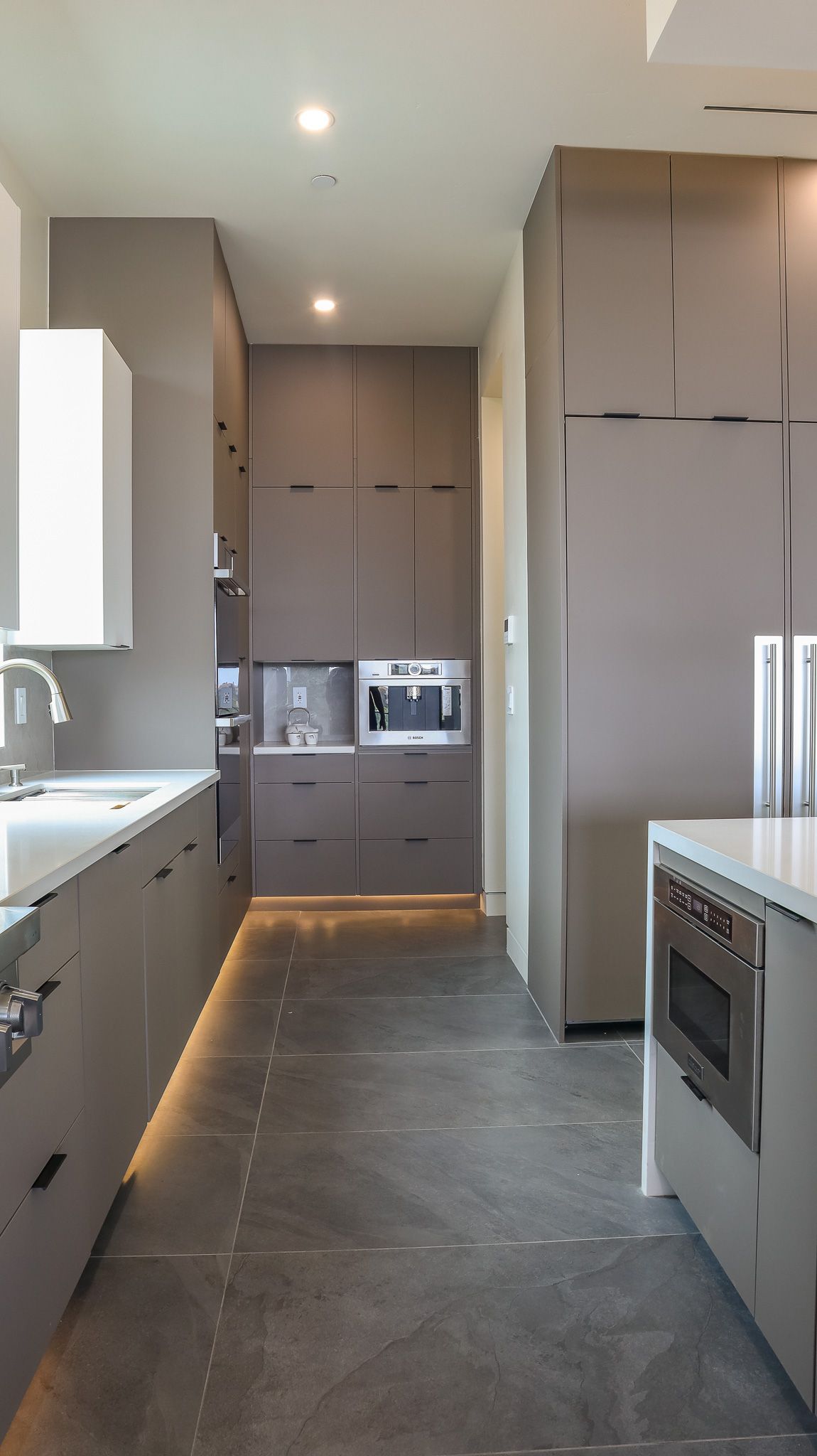 Modern kitchen with gray cabinets, island, stainless steel appliances, and dark flooring.