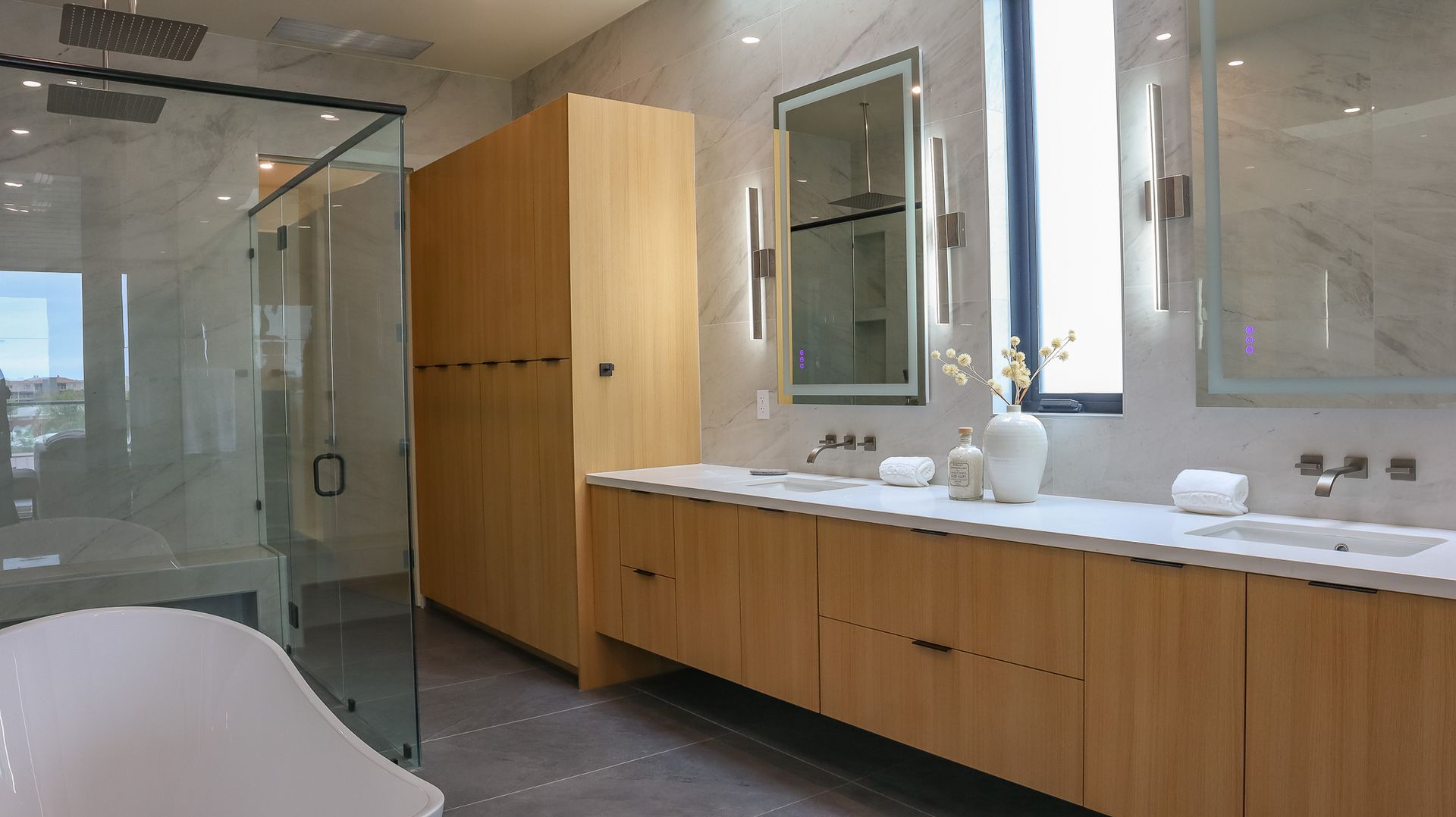 Modern bathroom with wood cabinetry, glass shower, and white countertops.