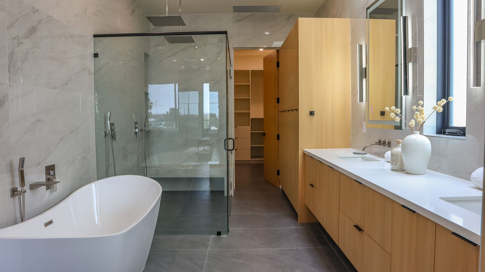 Modern bathroom with a bathtub, shower, wooden cabinets, and a walk-in closet.