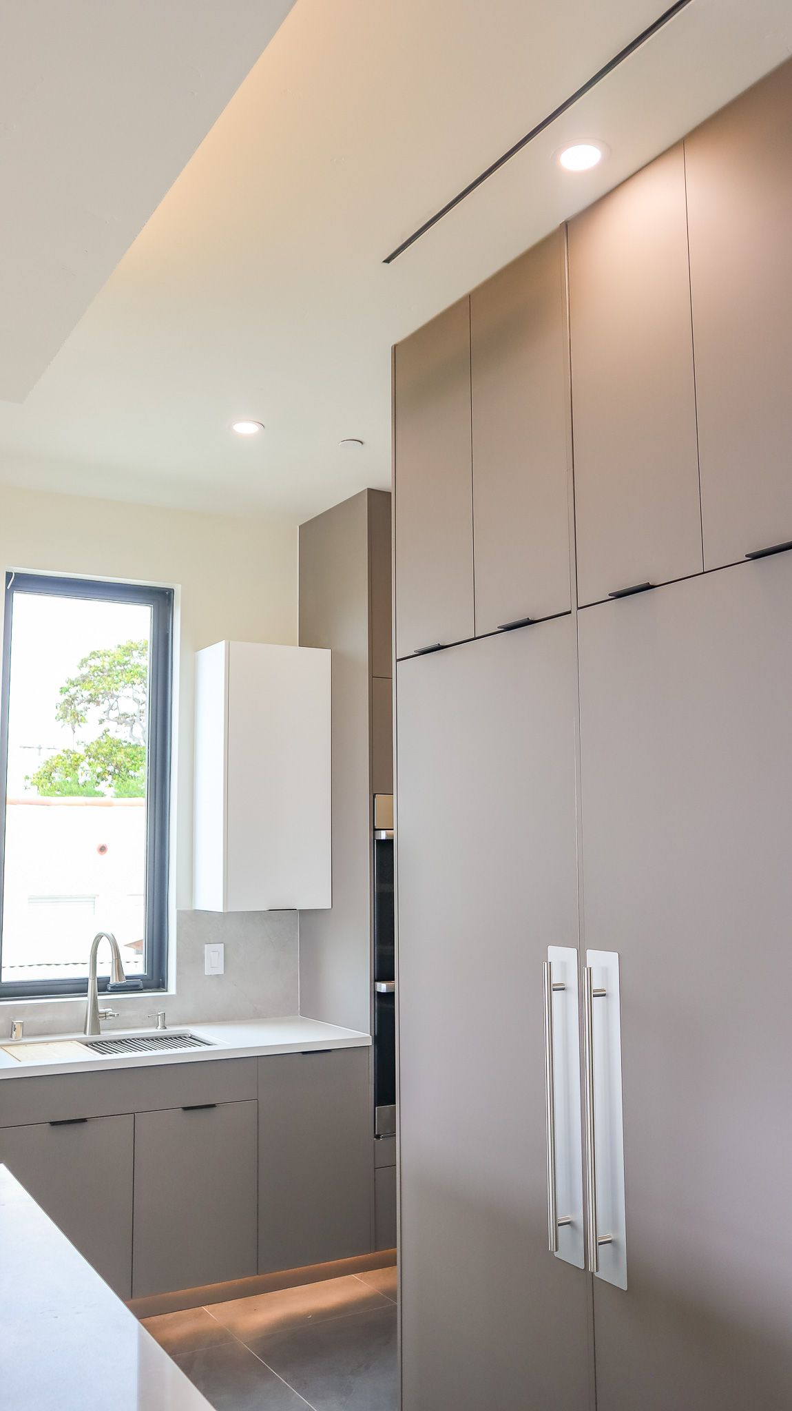 Modern kitchen interior with gray cabinets, a white countertop, and stainless steel appliances.