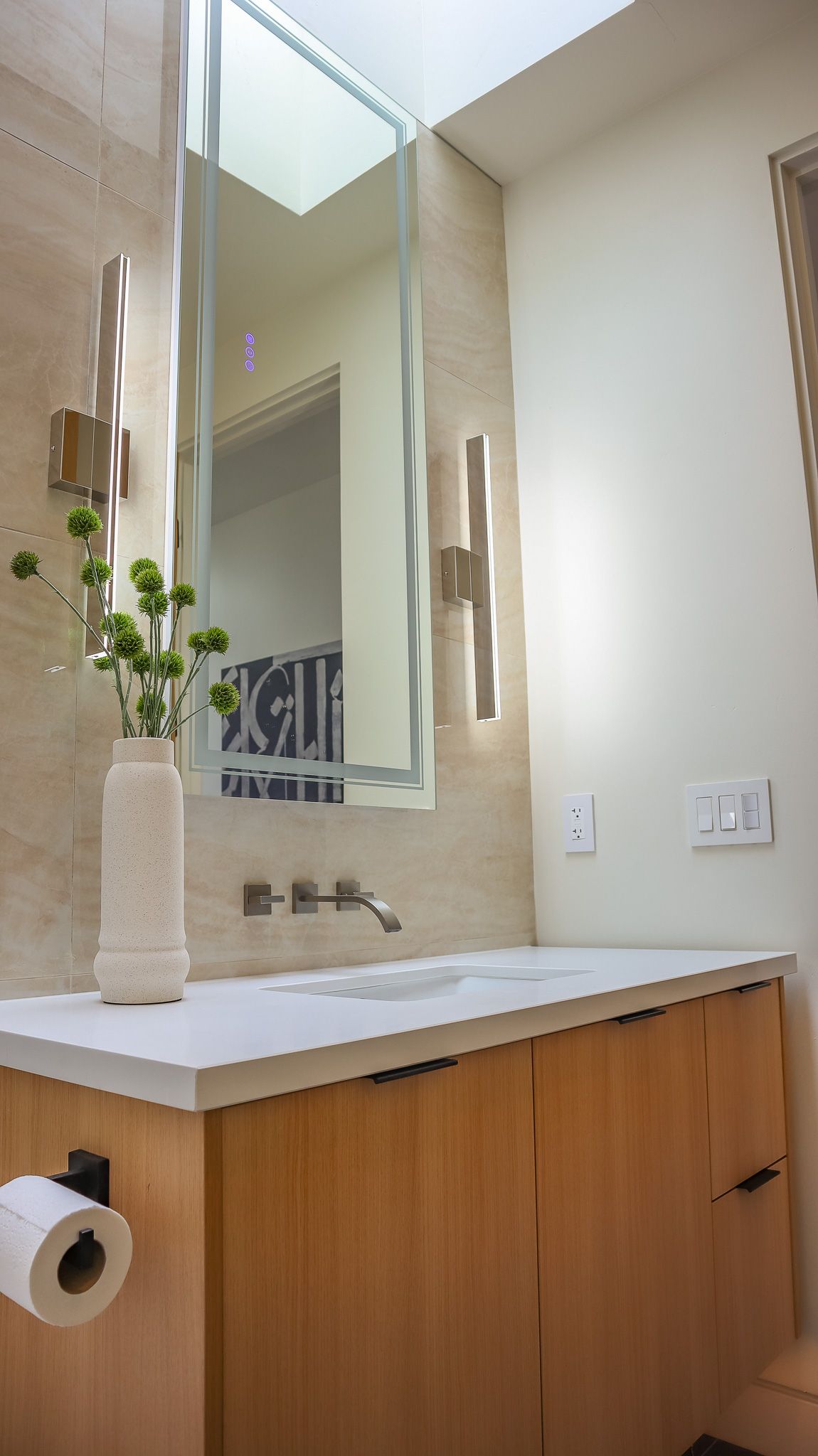 Bathroom with wooden vanity, white countertop, large mirror, and decorative lighting.