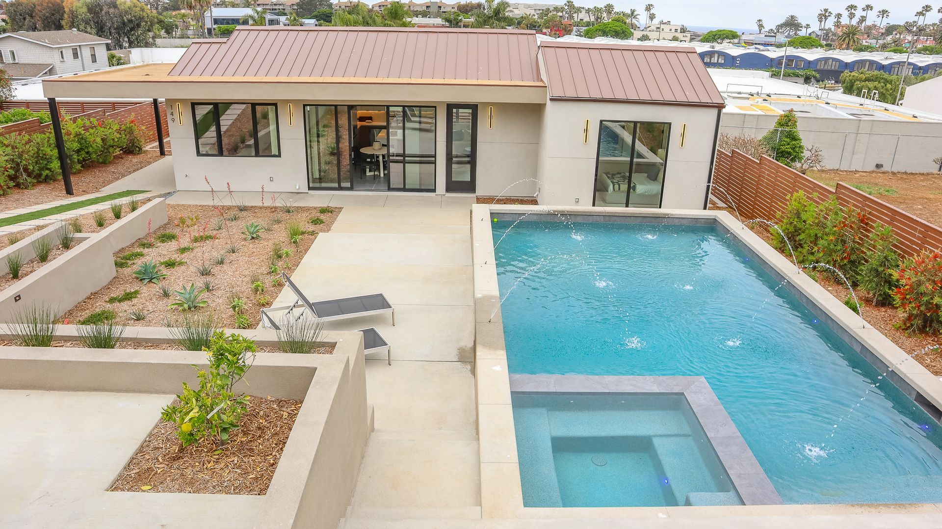 Backyard with a rectangular pool, spa, modern home with a brown roof, and landscaping.