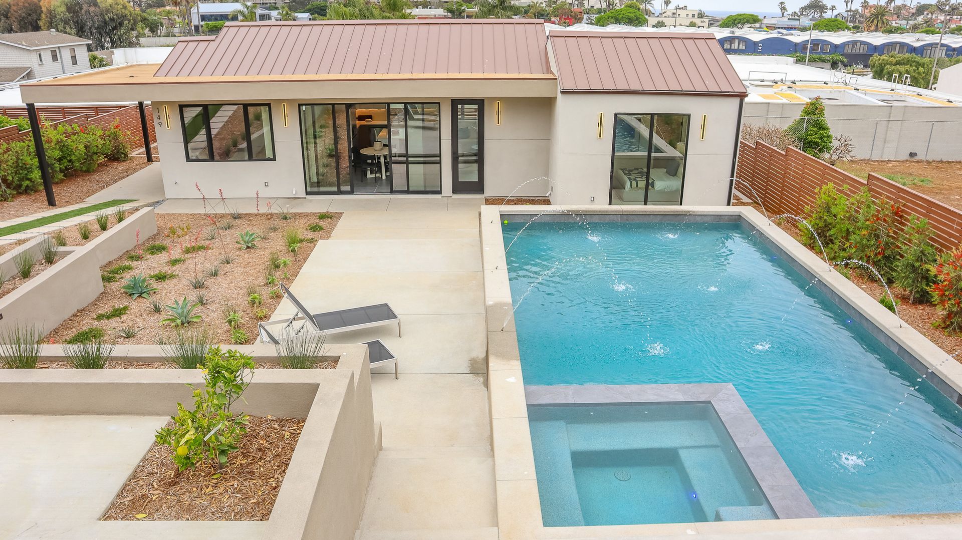 Modern home with a pool and patio. Tan exterior, bronze roof, and a rectangular pool.