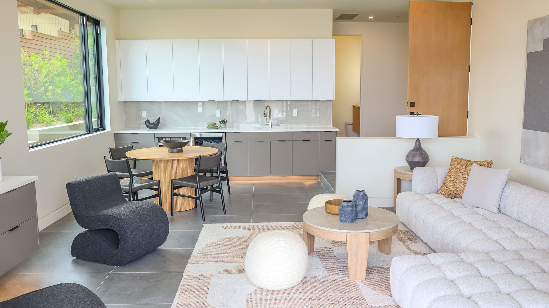 Modern living space with a kitchen, dining area, and living room featuring neutral colors and contemporary furniture.