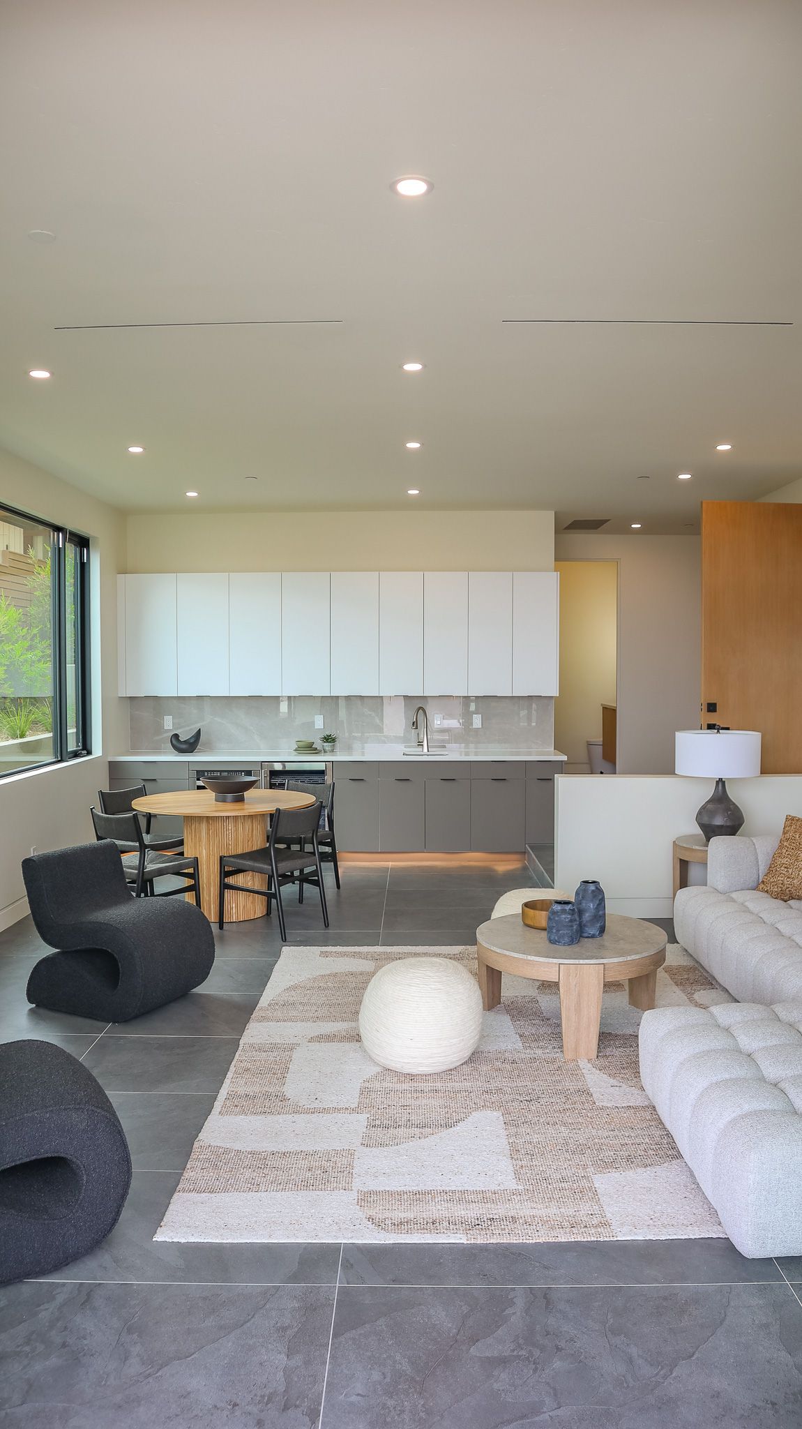 Open-concept living space with a kitchen, dining area, and living room; neutral colors with dark gray floors.
