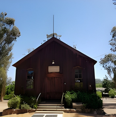 Historic wooden Olivenhain Meeting Hall surrounded by trees and open grounds.