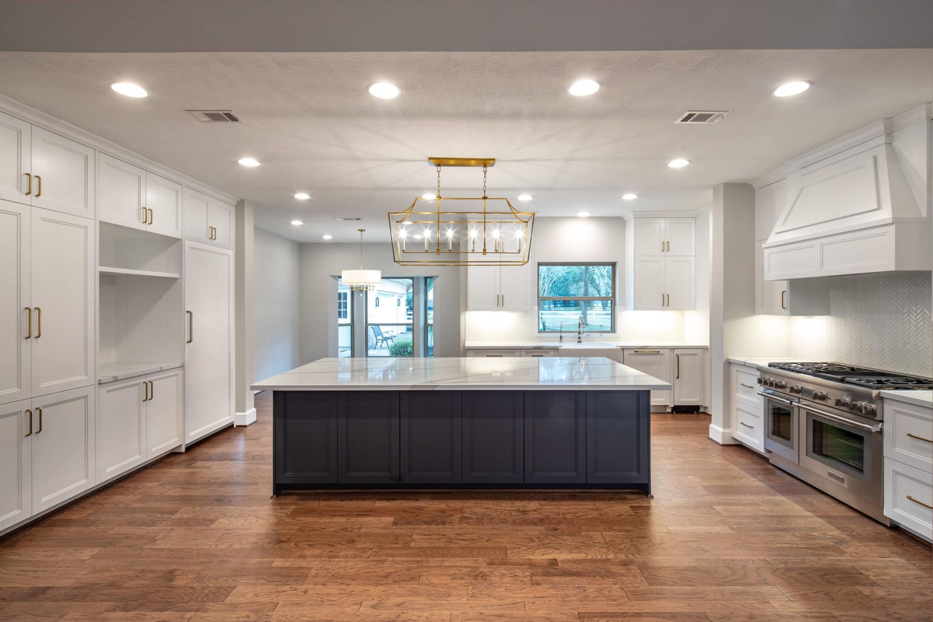 Spacious, modern kitchen with white cabinetry, navy island, stainless steel appliances, and wood flooring.