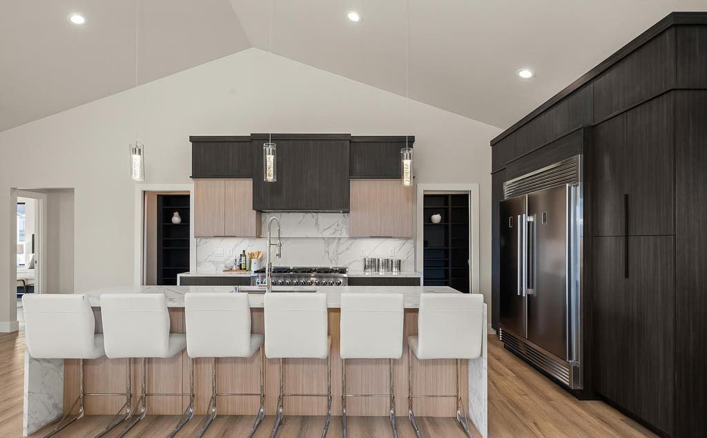 Modern kitchen with island seating, dark cabinets, stainless steel refrigerator, light wood floors.