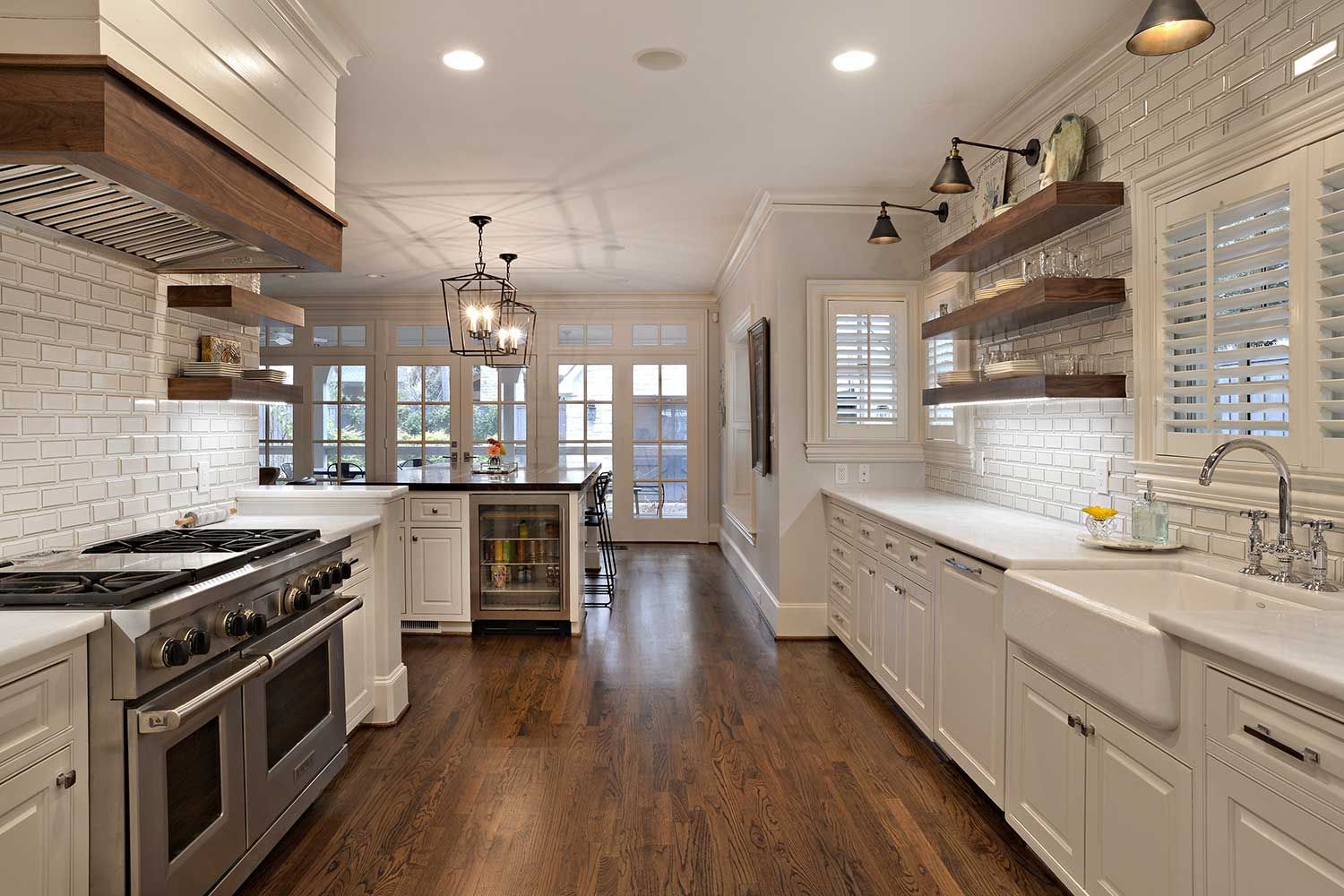 Elegant white kitchen with wood floors, stainless steel appliances, and open shelving.