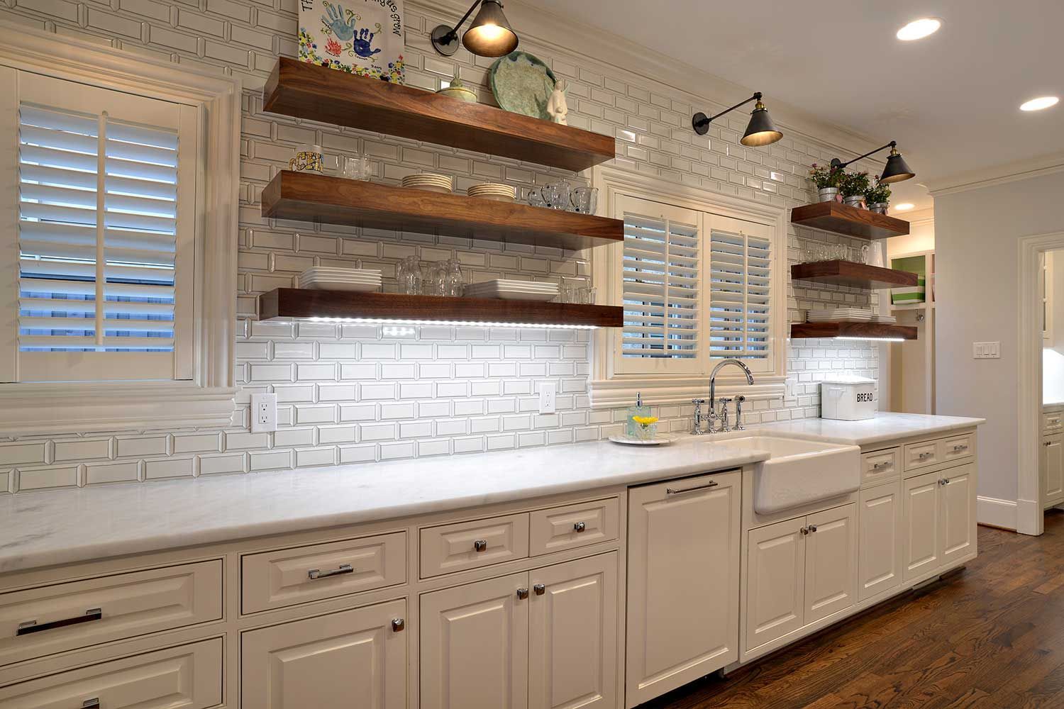 White kitchen with wood shelves, white brick backsplash, and white cabinets.