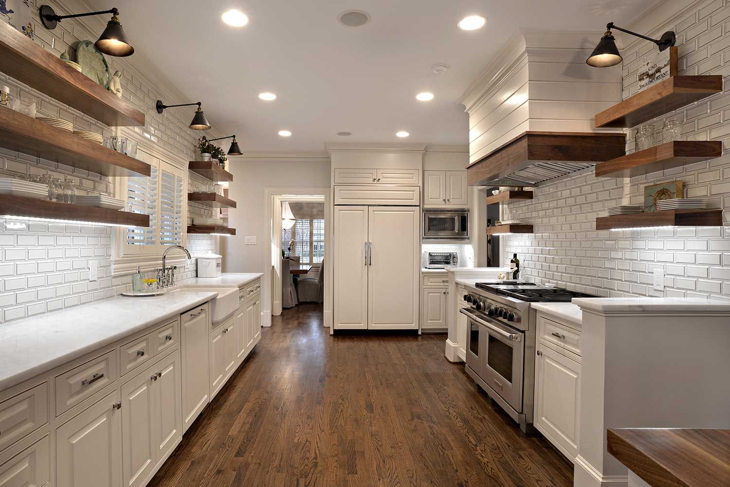 White kitchen with wood shelves, brick backsplash, stainless steel appliances, and dark wood floors.