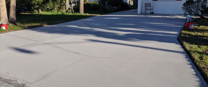 A concrete driveway leading to a house with trees in the background.