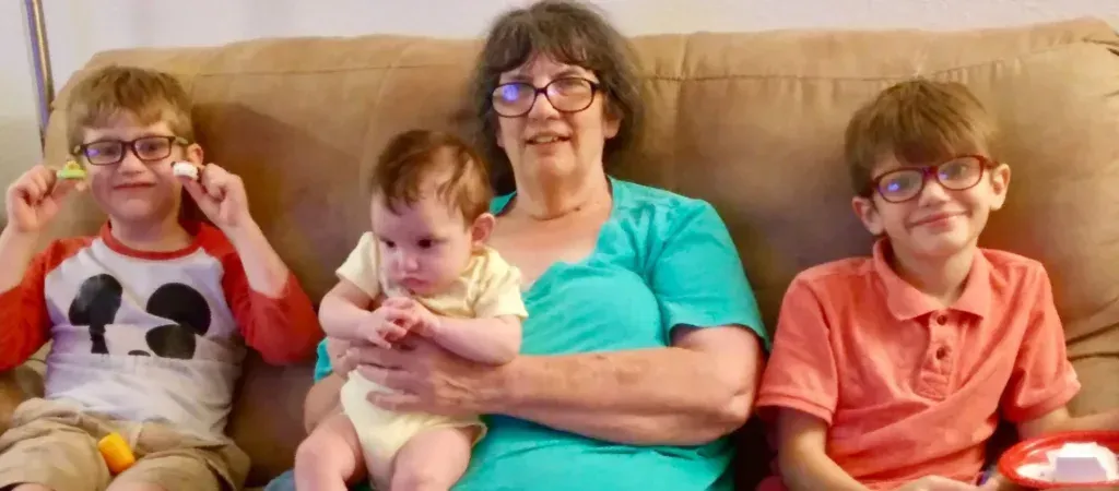 A woman is sitting on a couch holding a baby and two boys.