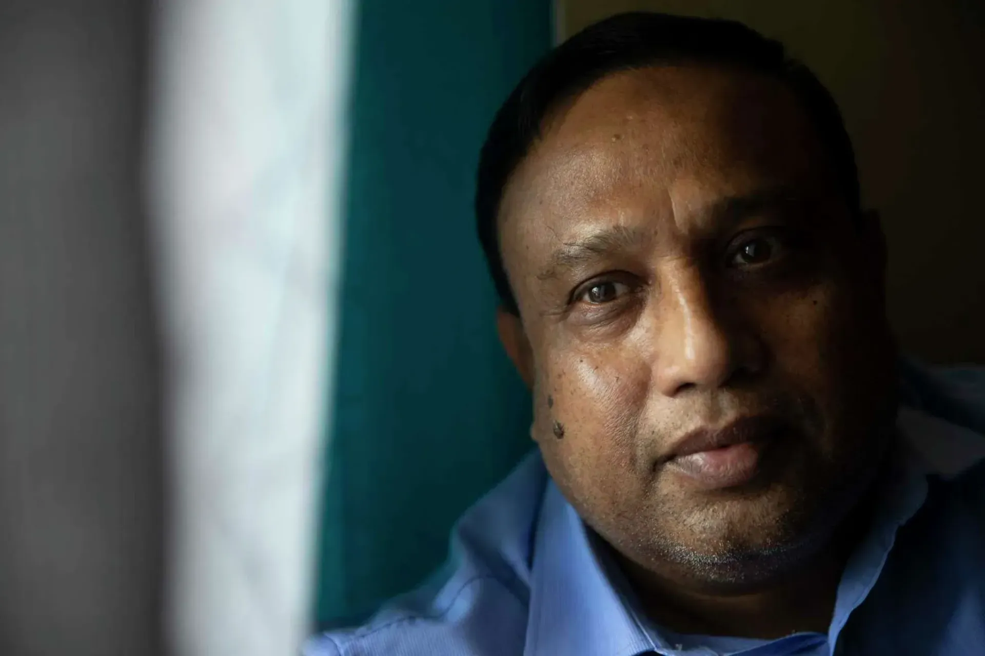 A man in a blue shirt is looking out of a window.