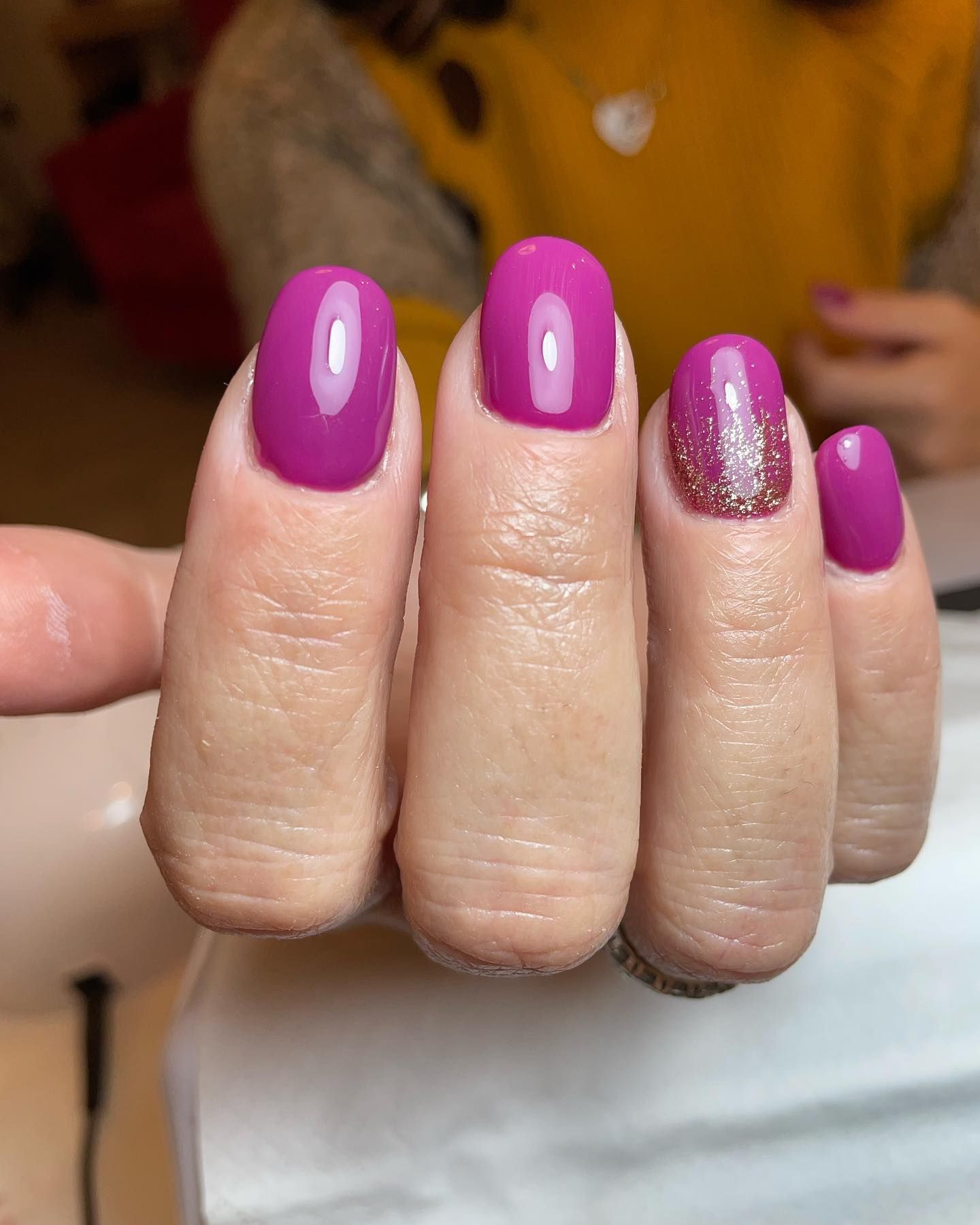 Primo piano di una mano con unghie ovali, curate color magenta. Un'unghia è decorata con glitter argentati.