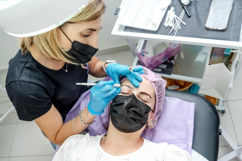 Persona sottoposta al trattamento delle sopracciglia; tecnico con mascherina e guanti che utilizza uno strumento; al chiuso.