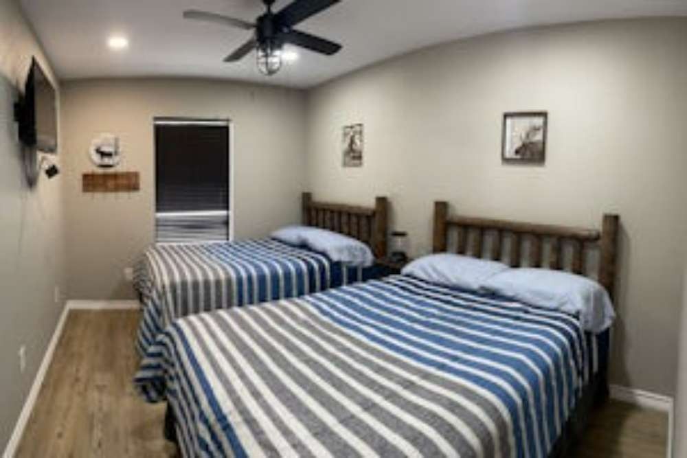 Two beds with blue and grey striped blankets in a bedroom with wood-framed beds and a ceiling fan.