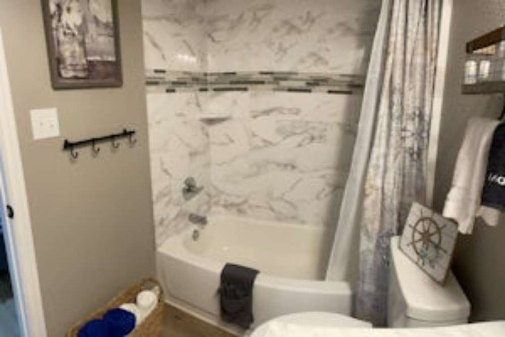 A bathroom with a marble-tiled shower, nautical-themed decor, and a toilet. A gray towel lies on the tub.