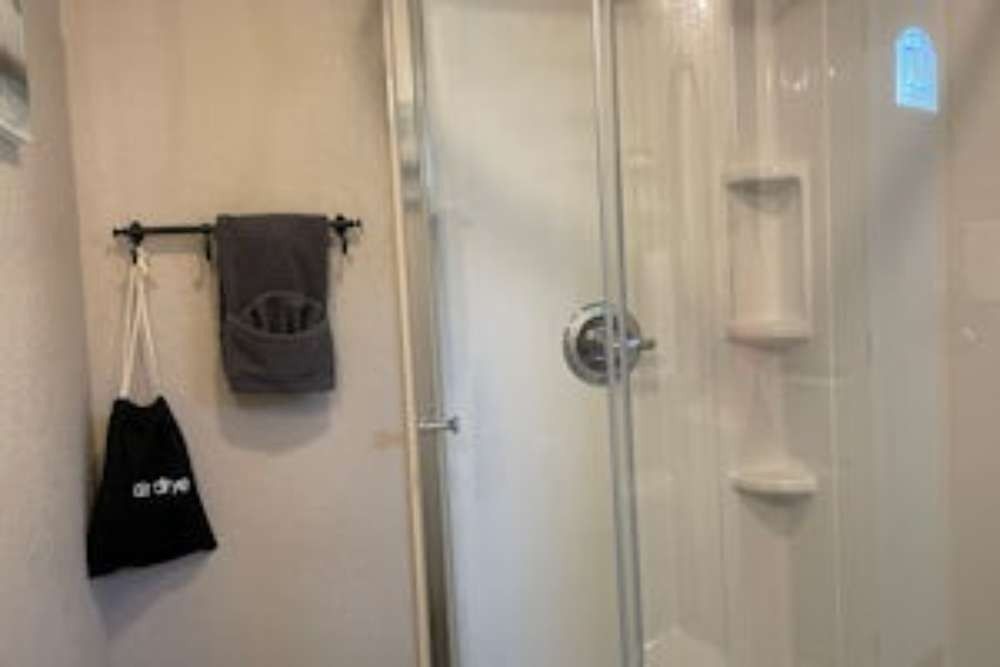 A small bathroom with a shower on the right and a towel rack with a towel and a bag on the left.