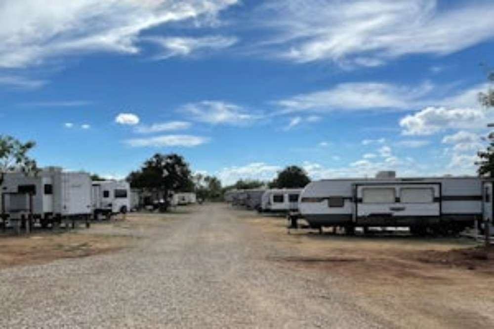 A gravel road lined with RVs under a bright blue sky with scattered clouds, suggesting a campground.