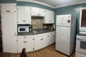 White kitchen with curved cabinets, a microwave, refrigerator, and stove. The walls are teal and the floor has a wood-look.
